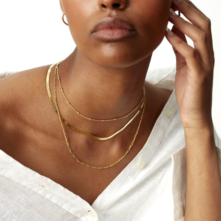 close up of model's neck wearing a gold bead chain choker necklace, a gold snake chain necklace and a gold figaro chain necklace